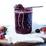 Small Batch Mixed Berry Jam straight on in mason jar with berries on the side and small spoon on top of jar.