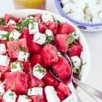 Watermelon salad with feta cheese in bowl behind and dressing in jar