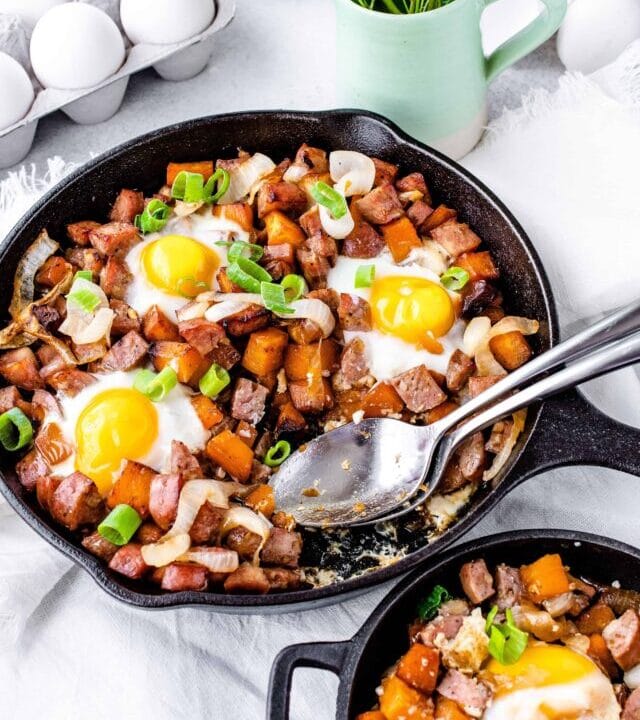 Image of caramelized onion sweet potato breakfast hash in a cast iron skillet with spoons scooping some out