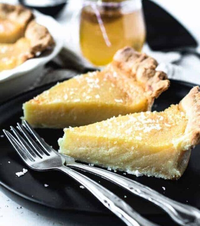 2 slices of salted honey pie on a black plate with 2 forks ready to eat