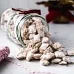 Jar of peppermint puppy chow spilling out on table with christmas tree behind