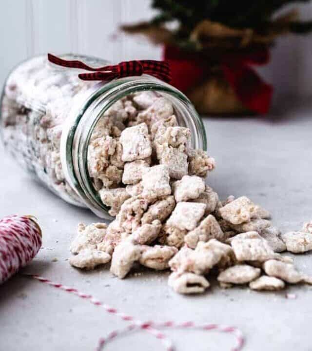 Peppermint puppy chow spilling from a jar with christmas tree in background