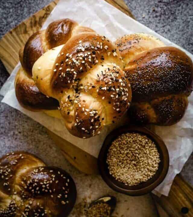 challah rolls on a cutting board with sesame seeds in a bowl