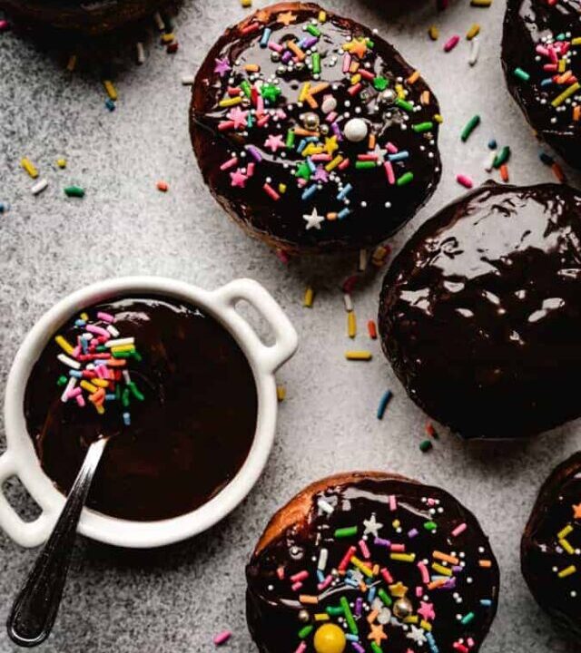 overhead of chocolate glazed donuts some with rainbow sprinkles and a bowl of chocolate glaze