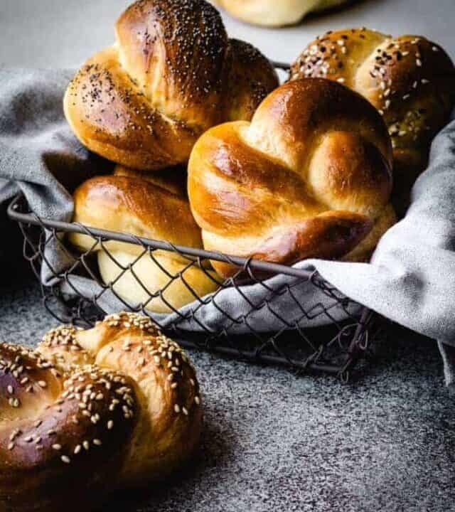 challah rolls in a bread basket with a grey napkin underneath