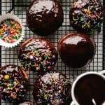 chocolate glazed donuts on a cooling rack with rainbow sprinkles and chocolate glaze in a bowl