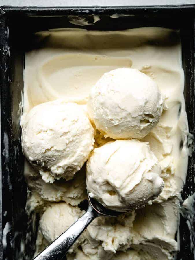 scoops of homemade vanilla ice cream in a pan with an ice cream scoop