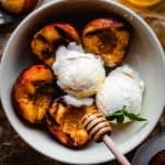 grilled peaches with scoops of vanilla ice cream being drizzled with honey