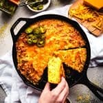 picking up a piece of jalapeno cheddar cornbread out of a cast iron skillet