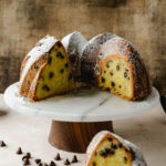 A slice of chocolate chip pound cake on a plate next to the cake display.