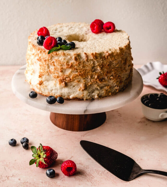 Berries a top an angel food cake sitting on a cake stand.