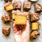 hand holding a piece of vanilla cake with chocolate frosting above other pieces with sprinkles