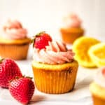 cupcake with frosting and strawberry on top with other cupcakes