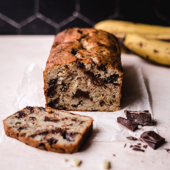 Banana bread sliced with chocolate chunks on the side and bananas behind.