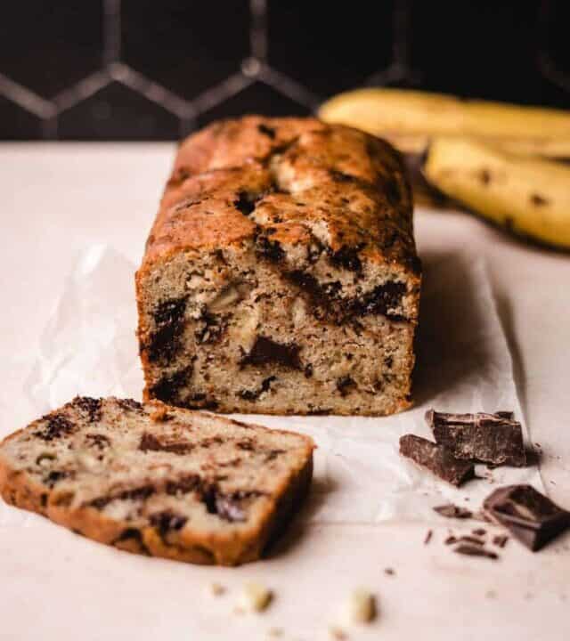 Banana bread sliced with chocolate chunks on the side and bananas behind.
