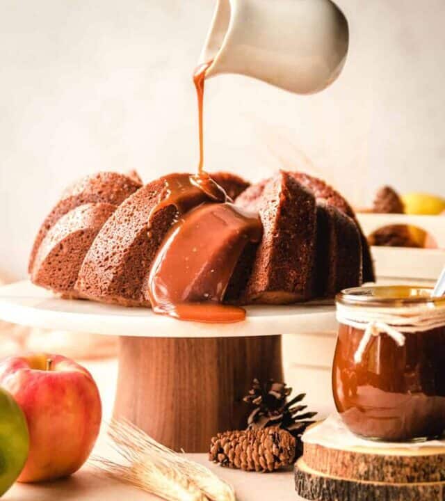 Apple spice cake on a cake stand with caramel being poured on top.