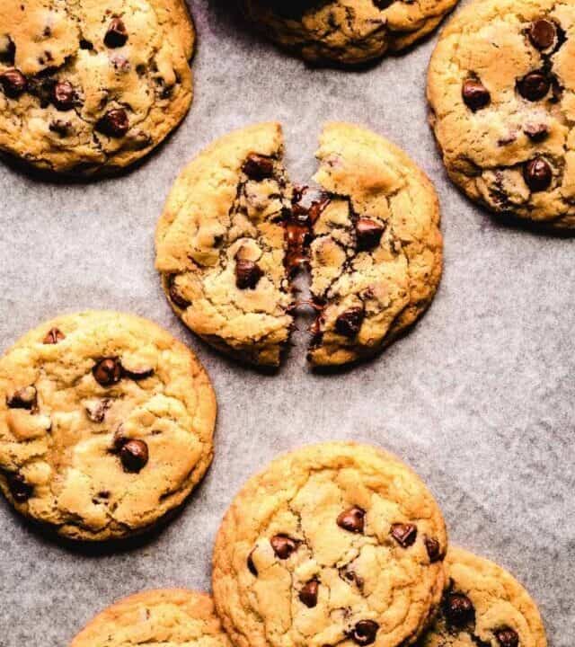 Top view of chocolate chip cookies without brown sugar sitting on parchment paper and melted chocolate coming out of two broken halves.