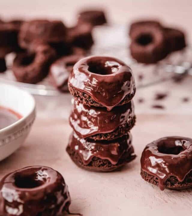 Freshly glazed mini chocolate donuts stacked on top of one another and a few sitting singly.