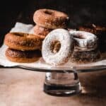 Variety of donuts on a cake pedestal, some of powdered sugar, others chocolate.