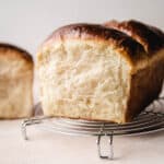Showing the side of a condensed milk bread loaf sitting on a cooling rack.