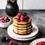 Small plate of self-rising pancakes with syrup dripping down over the stack onto the plate and fresh berries on top.
