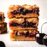 Large stack of cherry pie bars with fresh cherries in front.