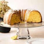 Half an Italian lemon pound cake sitting on a glass cake display with a glaze over it.
