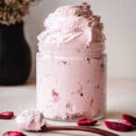Overflowing glass jar of strawberry marshmallow fluff and a spoon filled with fluff laying in front of the jar.