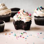 Bite taken out of a chocolate cupcake topped with frosting and sprinkles.