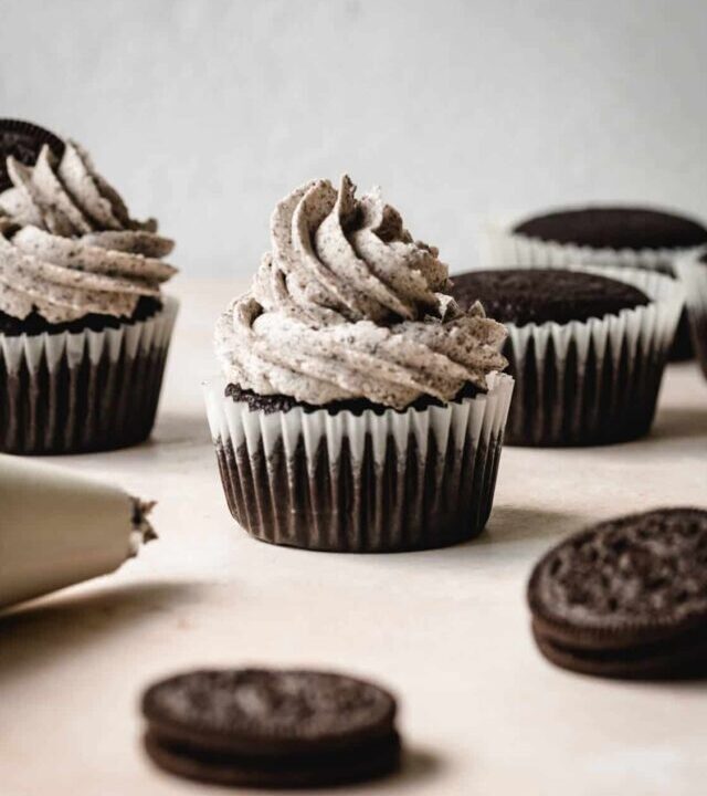 Oreo frosting on a chocolate cupcake sitting by the piping bag.