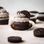 Oreo frosting topped chocolate cupcake with the wrapper pulled down sitting by oreo cookies.