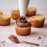 A frosting bag of dark chocolate buttercream frosting being added to a cupcake.