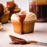 Salted caramel filled spoon sitting in front of a caramel buttercream frosted vanilla cupcake.