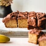 A banana cake cut up into squares of snack sized cake topped with chocolate frosting.