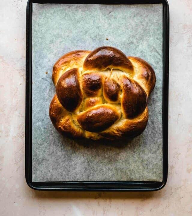 Baked round challah sitting on a parchment paper on a baking sheet