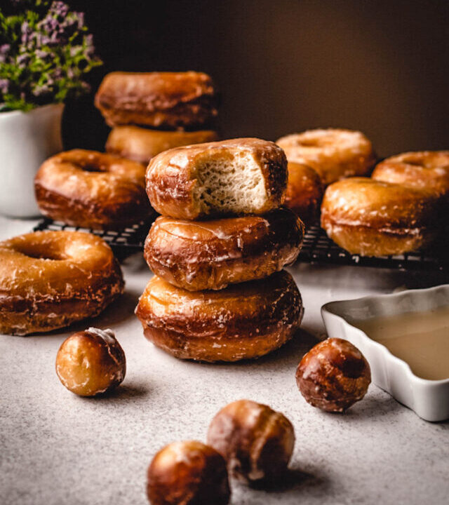 Glazed donuts stacked up with a bite taken out.
