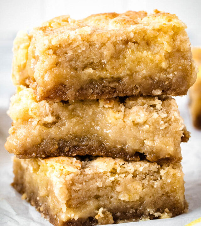 A stack of three lemon crumb bars with fresh lemon pieces by them.