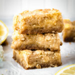 A stack of three lemon crumb bars with fresh lemon pieces by them.