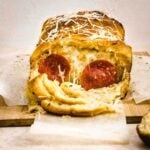 Freshly baked pull apart pizza loaf with a slice pulled away to reveal melty cheese and pepperoni slices.