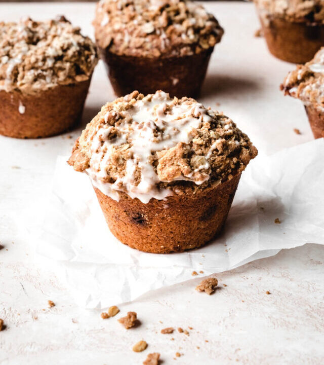 Several cinnamon streusel muffins on parchment paper covered with glaze.