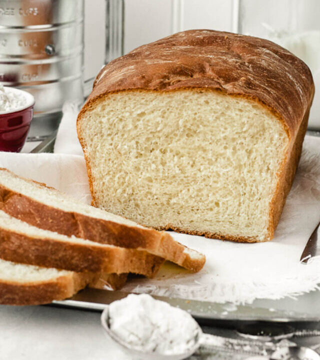 Tablespoon of flour sitting in front of a loaf of Amish white bread with a few slices laying next to it.
