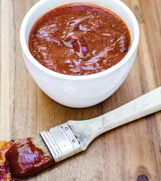 Basting brush full of sweet and spicy bbq sauce laying in front of the bowl.