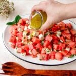 Hand pouring citrus mint dressing over a watermelon feta salad.