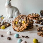 Mini egg cookies stacked with mini eggs garnished around it with a white bunny figurine in the background.
