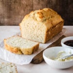 Loaf of 3-ingredient bread with a slice cut away in front of it and a bowl of butter.