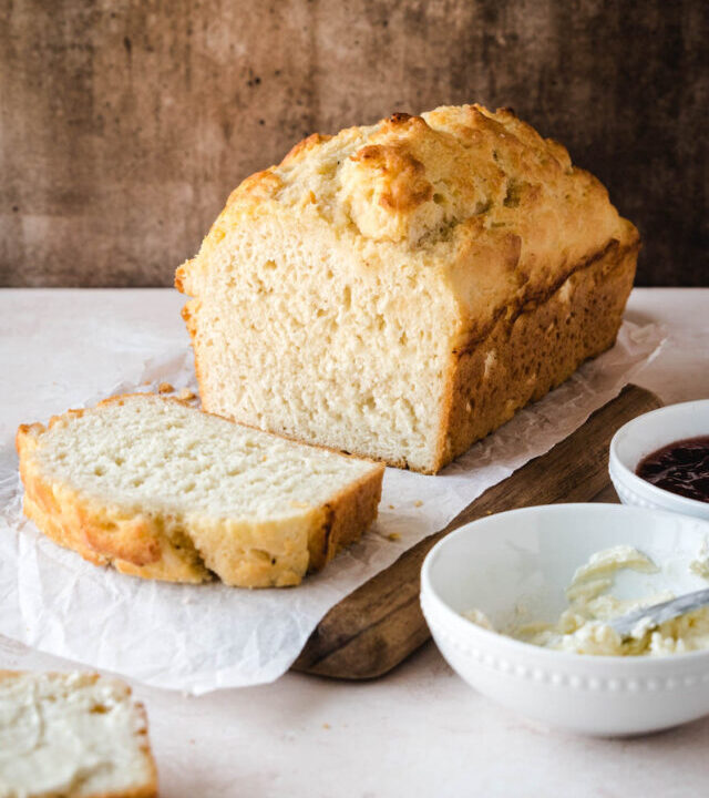 Loaf of 3-ingredient bread with a slice cut away sitting on a cutting board.
