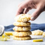 Hand stacking up 5 lemon crinkle cookies with lemon slices garnished around them.