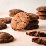 A chocolate sugar cookie is propped up against a stack of more cookies and some partially eaten and whole cookies scattered around them.