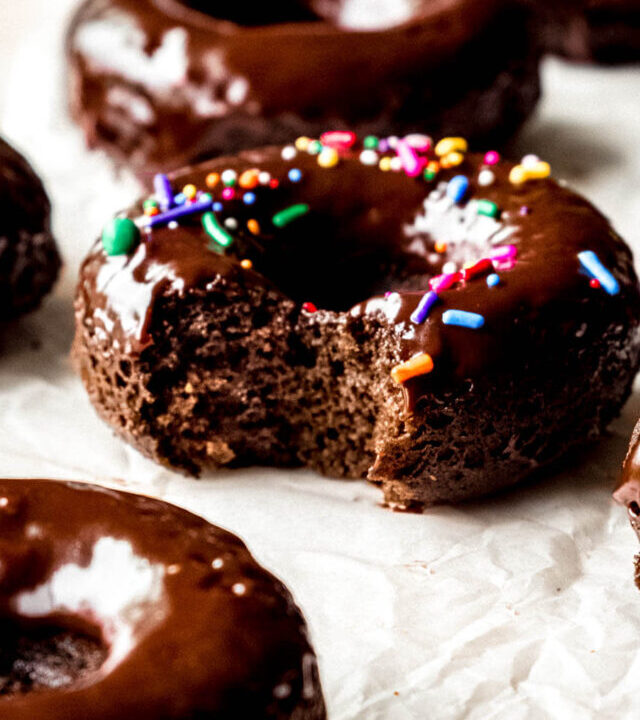 Baked chocolate donuts with a rich chocolate glaze and sprinkles, with a bite missing.