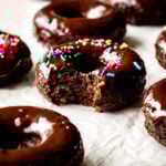 Baked chocolate donuts with a rich chocolate glaze and sprinkles, with a bite missing.